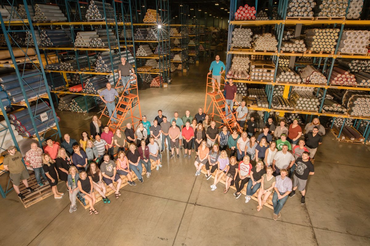 Employees at TVF sit and stand among large stacks of pipes for their employee ownership month photo.